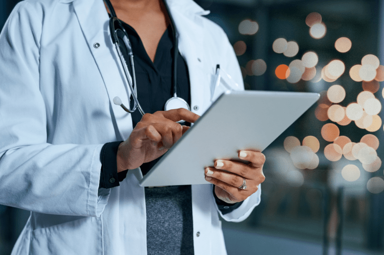 A female doctor in a white coat holds a tablet, symbolizing IT compliance in healthcare.
