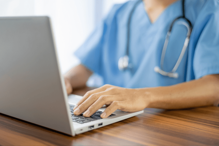 A doctor typing on a laptop, focusing on healthcare IT security measures.